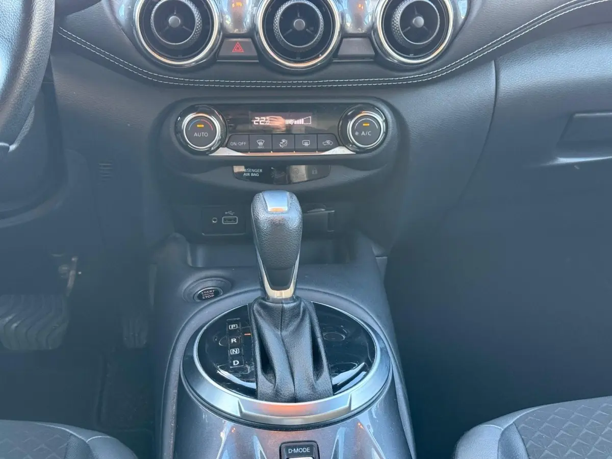 Vue intérieure centrée sur la console centrale noire du Nissan Juke 2023 avec levier de boîte auto et commandes climatisation.