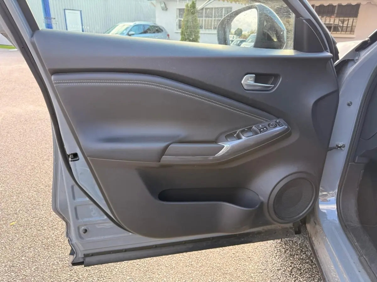 Vue intérieure de la porte avant gauche gris clair du Nissan Juke 2023 avec commandes électriques et haut-parleur intégré.