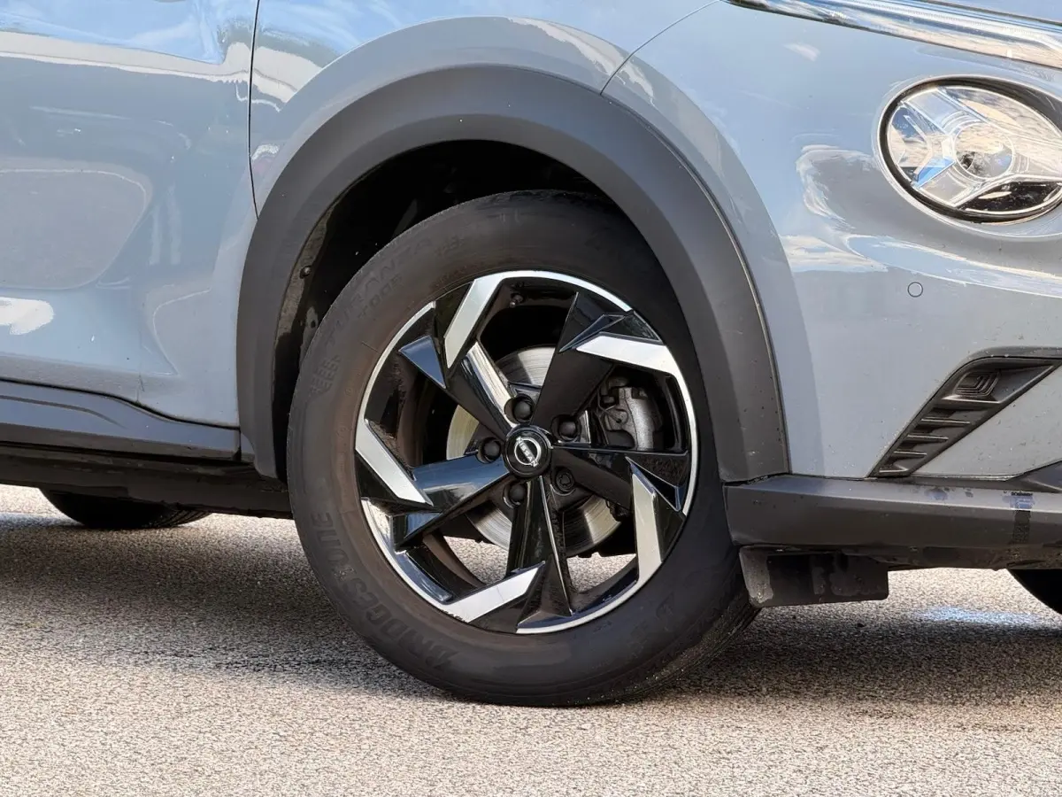 Gros plan sur la roue avant droite et le phare d'un Nissan Juke gris clair avec jante noire et argentée.