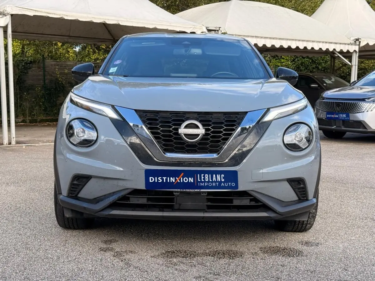 Vue de face d'un Nissan Juke gris clair 2023 avec calandre en V chromée et phares ronds LED distinctifs.