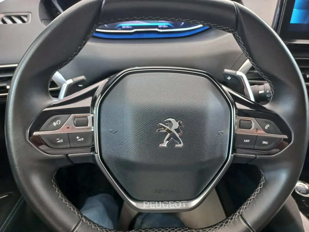 Volant cuir noir de Peugeot 5008 2021 avec commandes multifonctions et logo lion au centre, vue de face rapprochée.