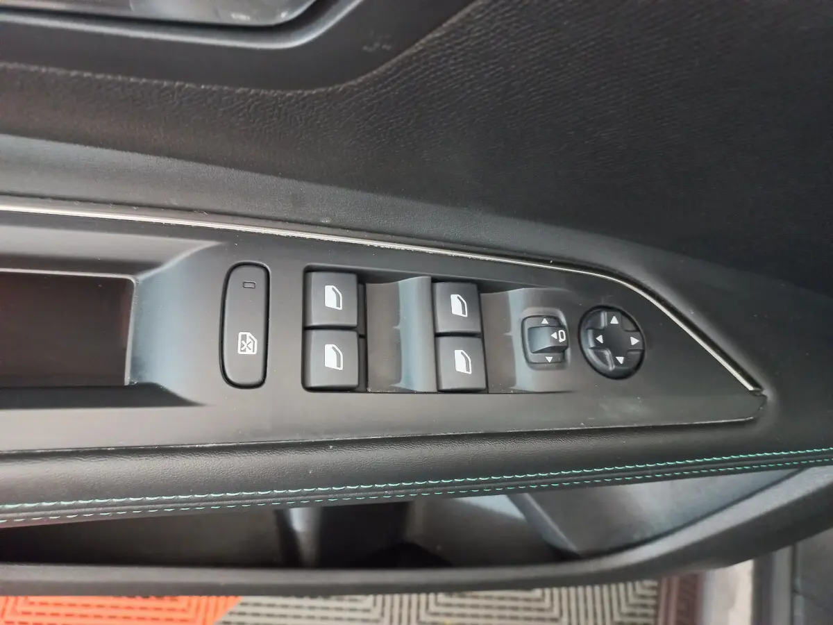 Gros plan sur la commande des vitres et rétroviseurs côté conducteur du Peugeot 5008 gris foncé, avec surpiqûres bleues.