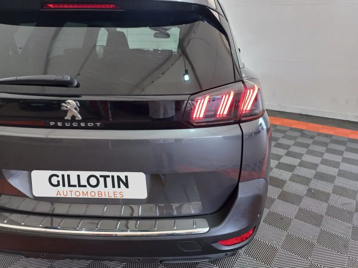 Vue arrière droite d'un Peugeot 5008 gris foncé avec feux arrière LED allumés et logo Peugeot visible.