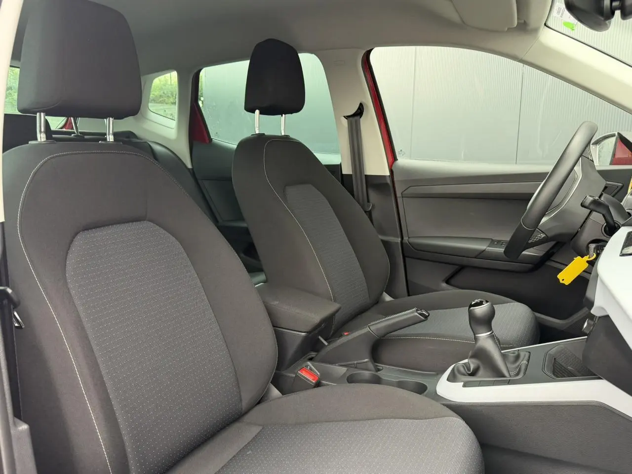 Vue intérieure côté conducteur du SEAT Arona rouge, mettant en valeur les sièges avant en tissu noir et la boîte manuelle.