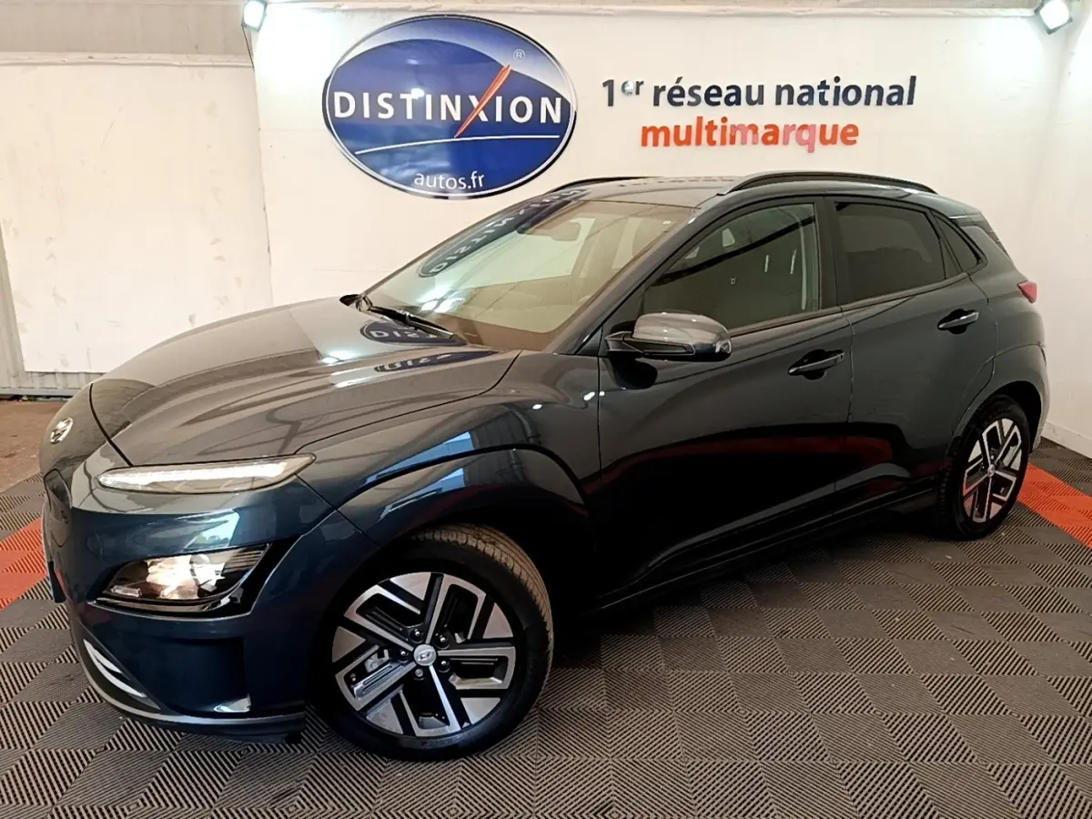 Hyundai Kona électrique bleu en 3/4 avant droit, avec jantes alliage et rétroviseurs chromés dans un showroom.