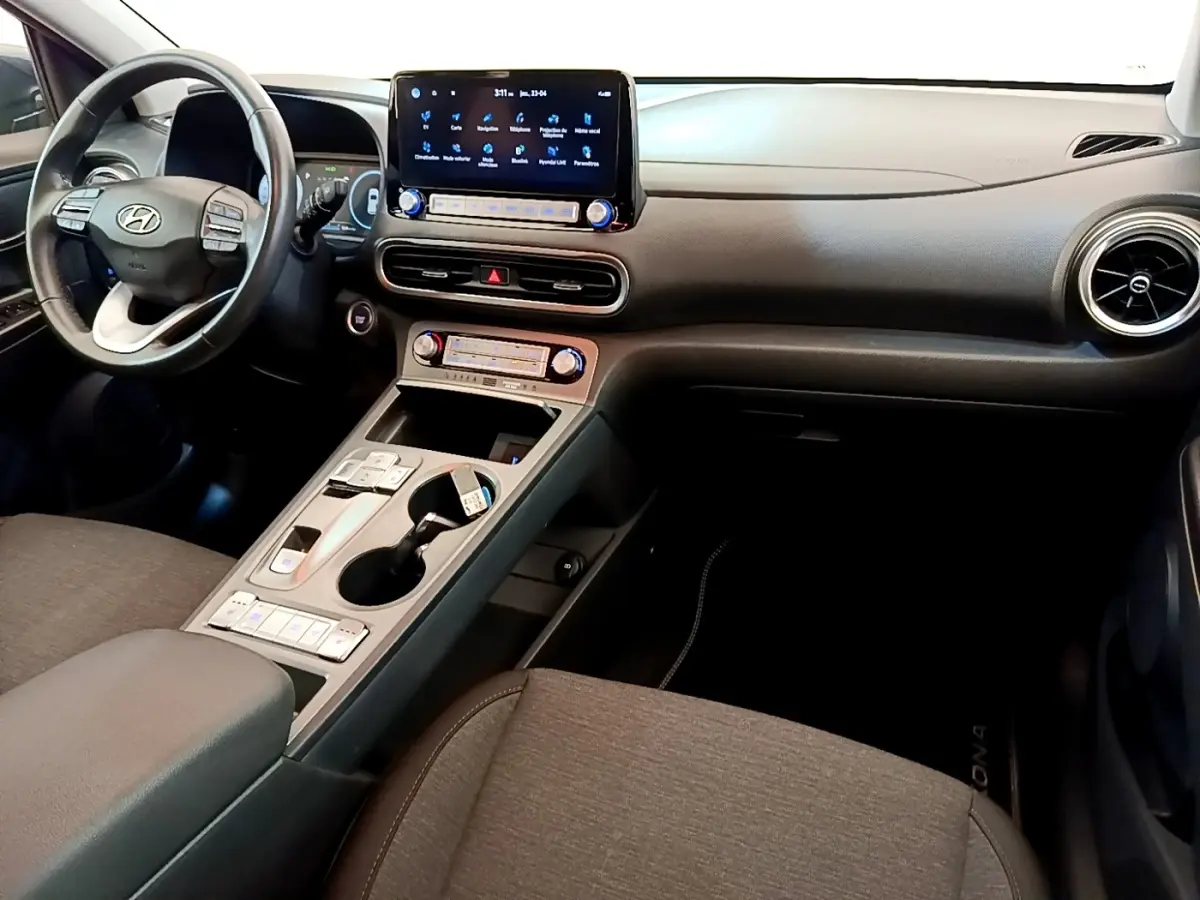 Vue intérieure avant droite du Hyundai Kona électrique 2023, tableau de bord noir avec écran tactile central et volant cuir multifonctions.