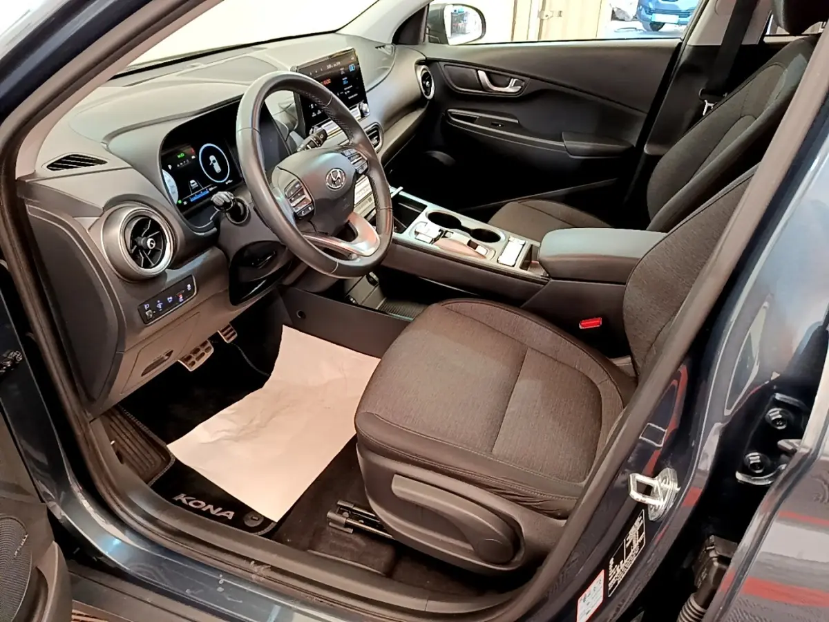Vue intérieure côté conducteur du Hyundai Kona électrique 2023 bleu, avec volant cuir multifonctions et tableau de bord digital.
