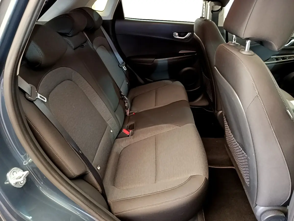 Vue intérieure côté arrière gauche du Hyundai Kona électrique 2023, montrant la banquette arrière en tissu gris et noir.