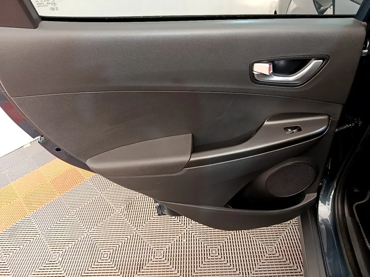 Vue intérieure de la porte arrière droite du Hyundai Kona bleu 2023 avec panneau noir et commande de vitre électrique.