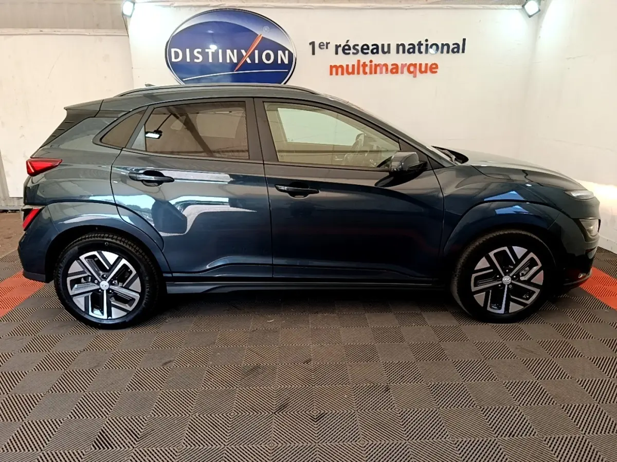 Vue latérale gauche d'un Hyundai Kona électrique bleu 2023 avec jantes alliage et rétroviseurs noirs.