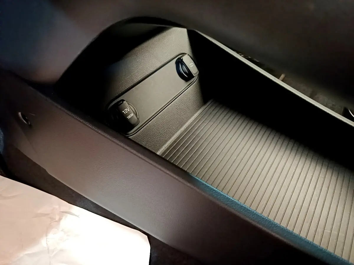 Gros plan sur la console centrale noire du Hyundai Kona électrique 2023 avec prise 12V et port USB.