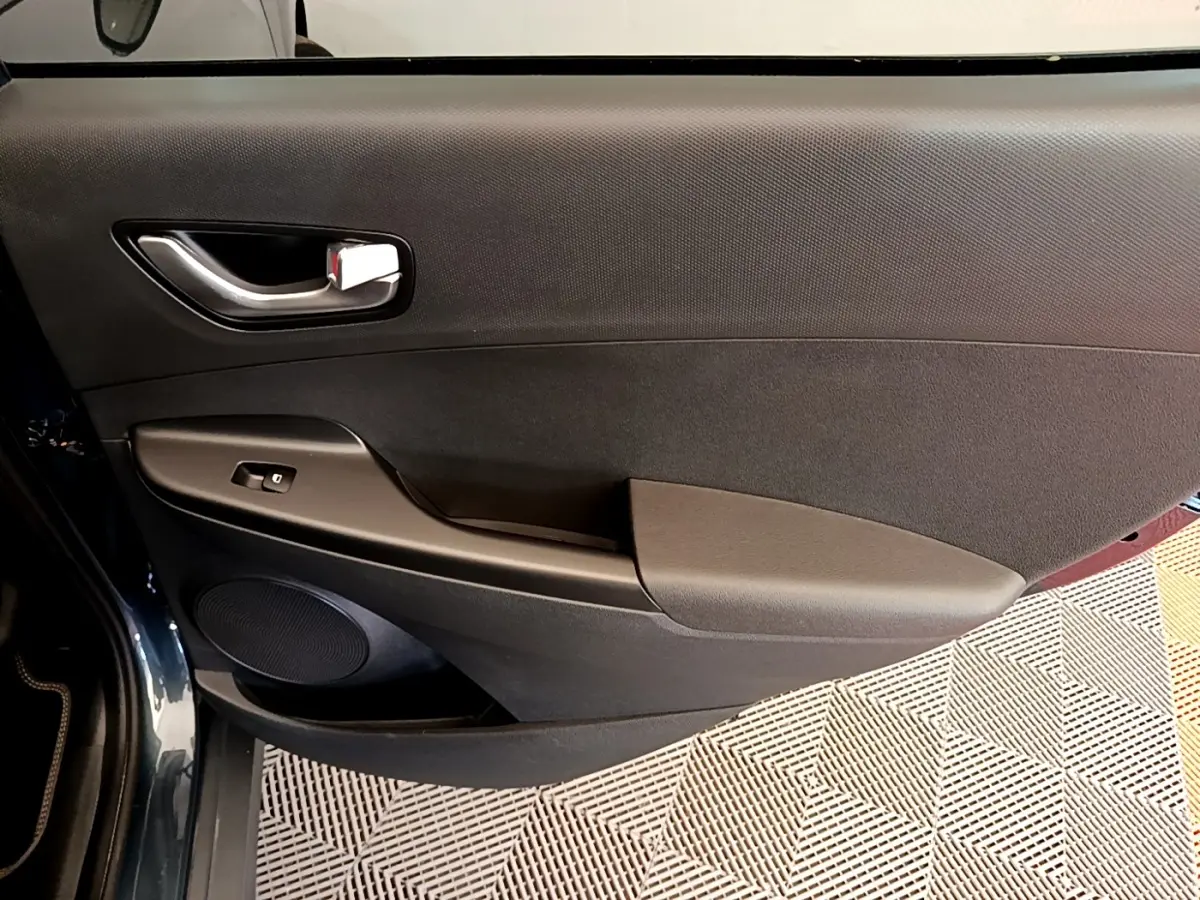 Vue rapprochée de la porte avant gauche noire du Hyundai Kona électrique 2023 avec poignée argentée et commande de vitre.