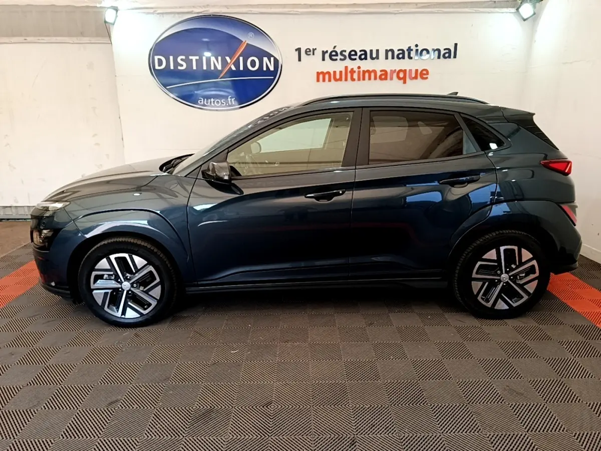 Vue latérale droite d'un Hyundai Kona électrique bleu 2023, avec jantes modernes et toit noir contrasté.