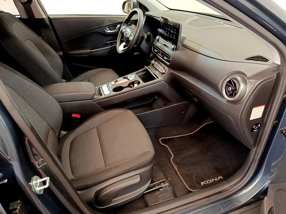Vue intérieure côté conducteur de la Hyundai Kona électrique 2023 bleu, avec volant cuir multifonctions et tableau de bord moderne.