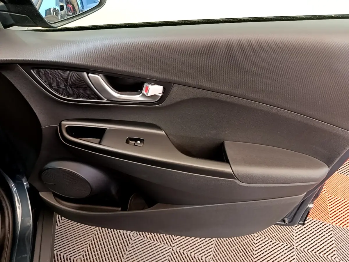 Vue rapprochée de la porte intérieure côté gauche bleu foncé du Hyundai Kona électrique avec poignée argentée et haut-parleur intégré.