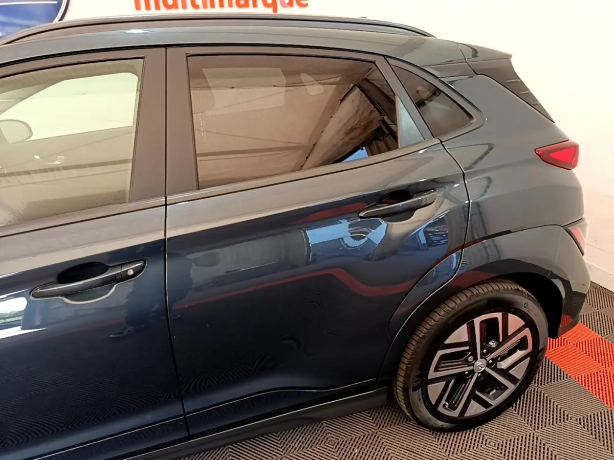 Vue latérale droite d'un Hyundai Kona électrique bleu foncé avec jantes spécifiques et poignées de porte intégrées.