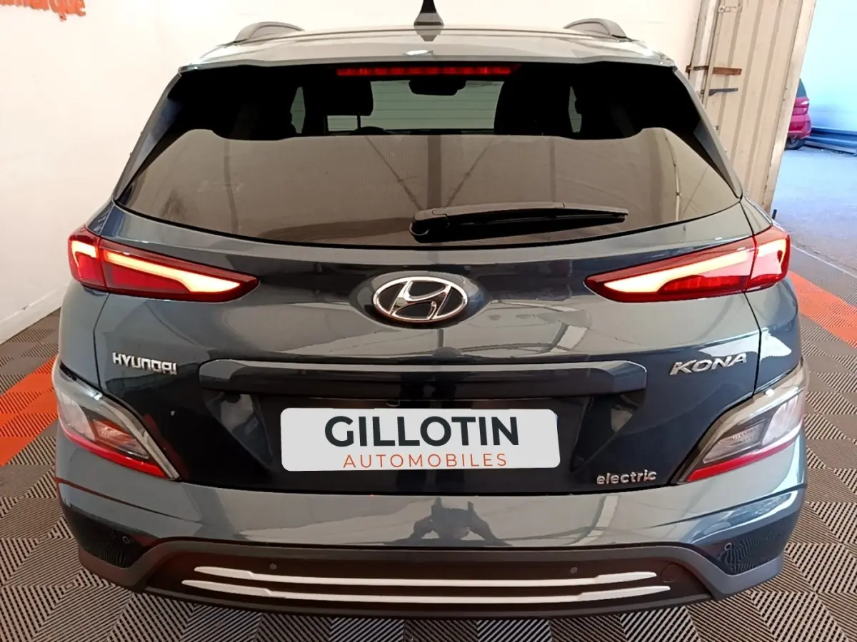 Vue arrière d'un Hyundai Kona électrique bleu avec feux LED allumés et logo visible sur un sol à damier rouge et noir.