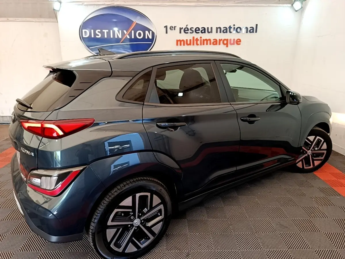 Vue 3/4 arrière droite d’un Hyundai Kona électrique bleu 2023 avec feux LED et jantes distinctives en intérieur showroom.