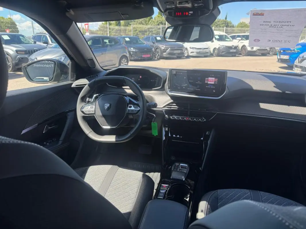 Vue intérieure avant du Peugeot 2008 Hybrid noir, montrant le volant compact, l'écran tactile central et les sièges tissu.