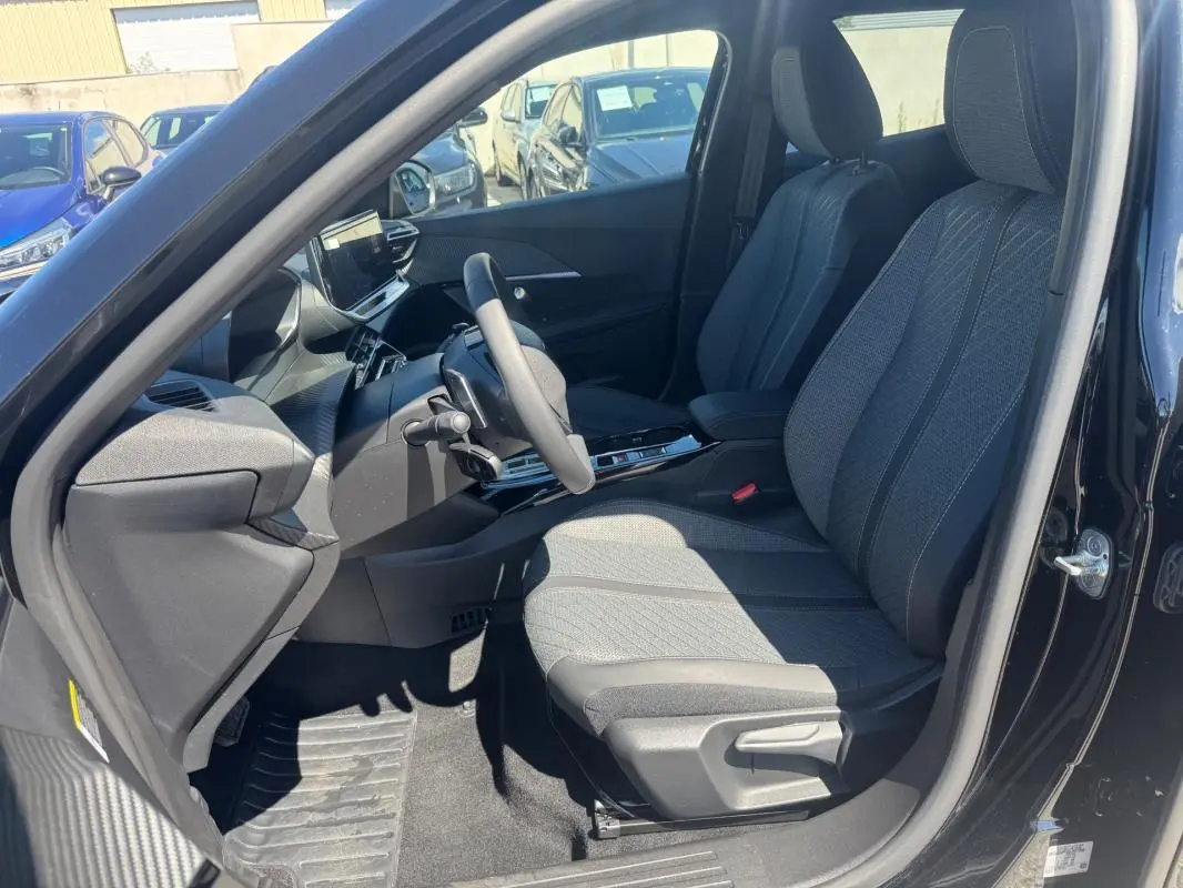 Vue intérieure côté conducteur du Peugeot 2008 Hybrid noir 2025, sièges tissu gris et tableau de bord moderne avec écran tactile.