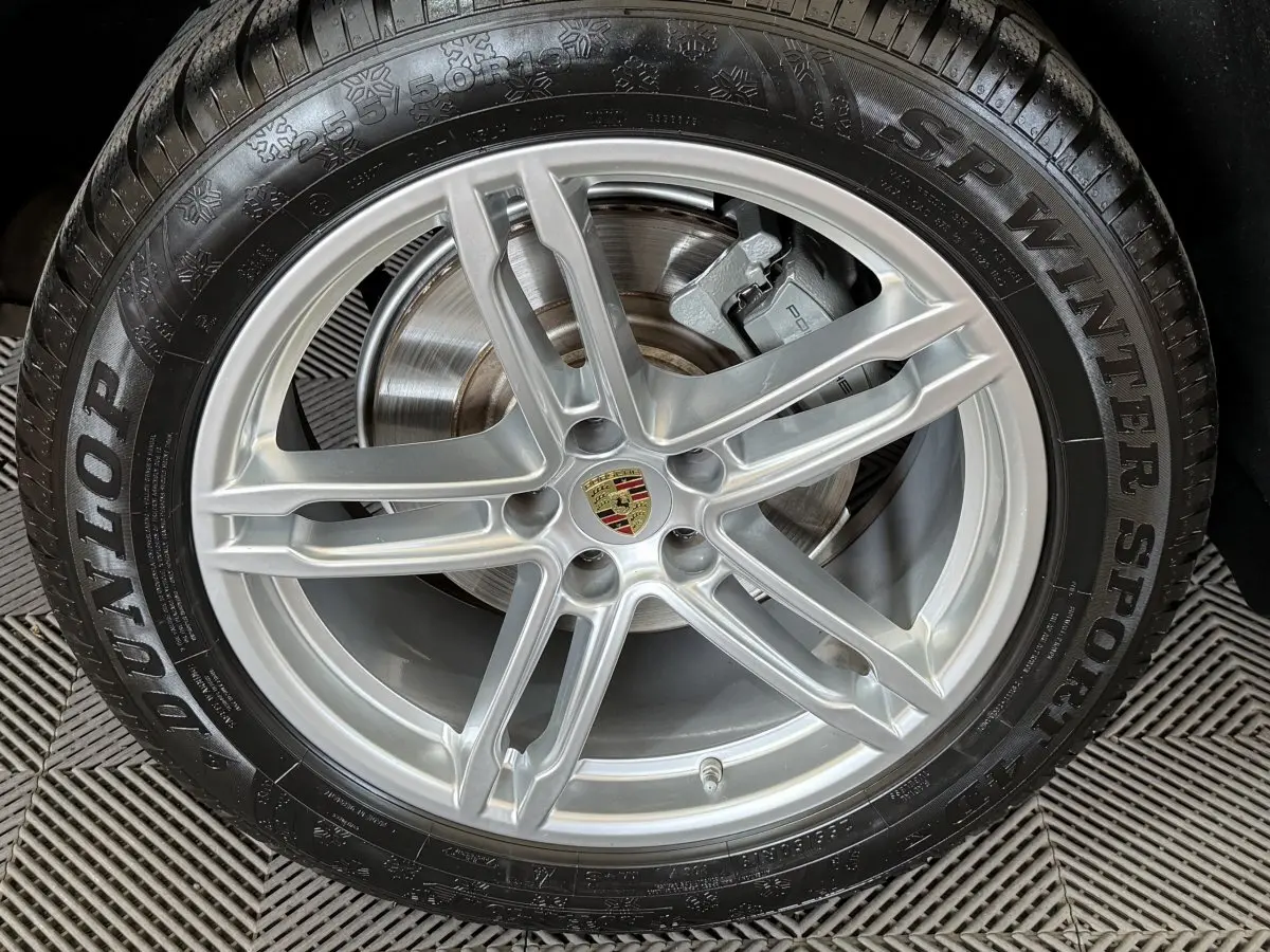Gros plan sur la jante alu argentée avec logo Porsche au centre, montée sur pneu hiver Dunlop SP Winter Sport.