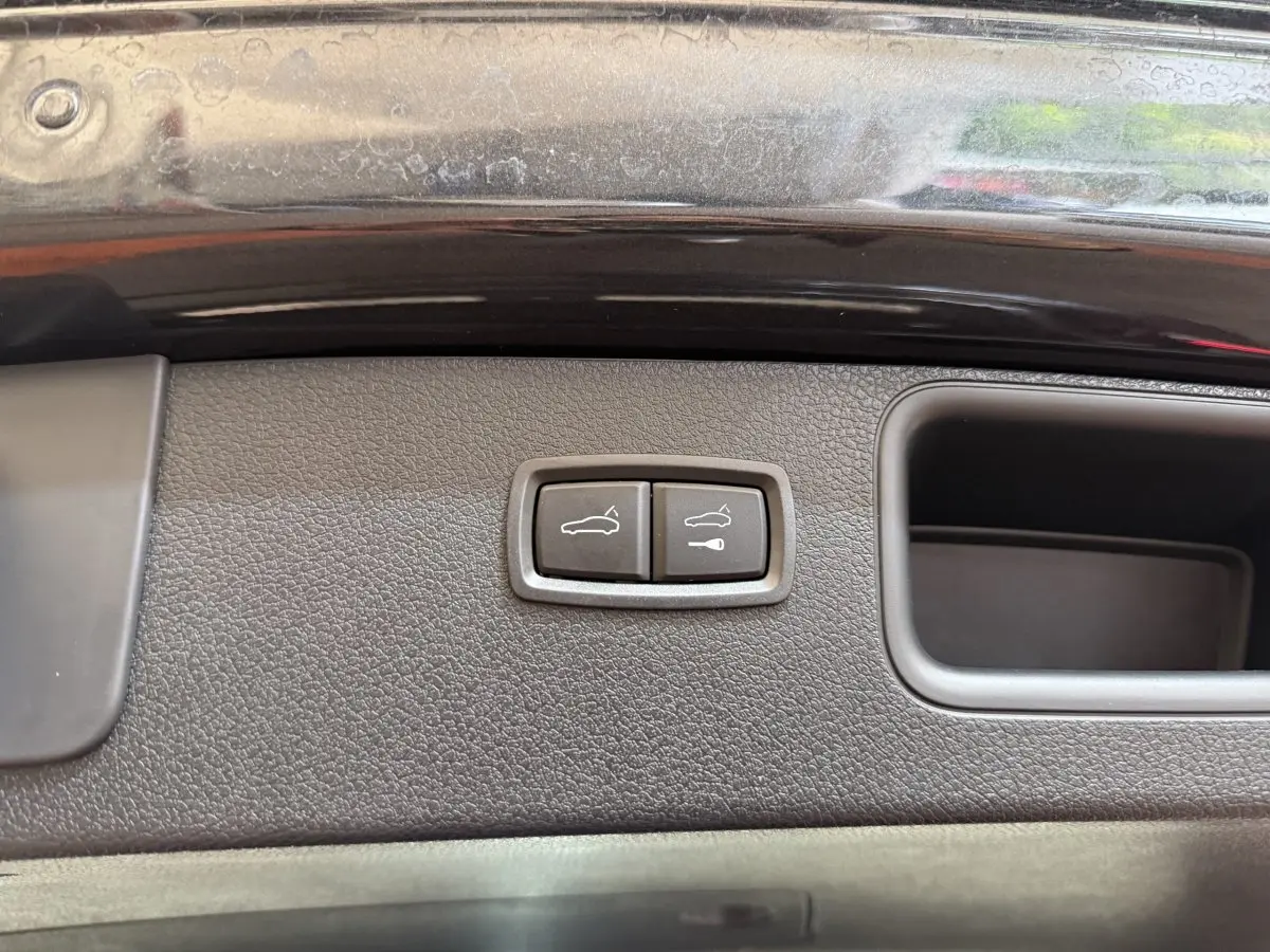 Gros plan sur les boutons d'ouverture électrique du coffre sur la porte arrière d'un Porsche Macan gris foncé.