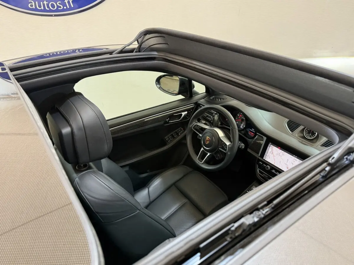 Vue intérieure par le toit ouvrant du Porsche Macan 3.0 S gris foncé, volant cuir alu et écran tactile de navigation visible.