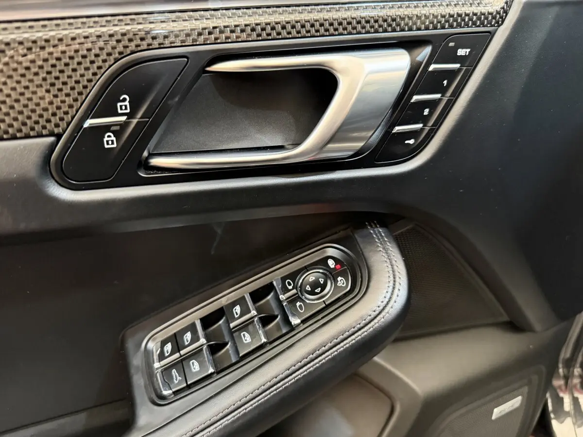 Gros plan sur la porte côté conducteur du Porsche Macan 3.0 S gris foncé, avec commandes alu et cuir, boutons mémoire et vitres.