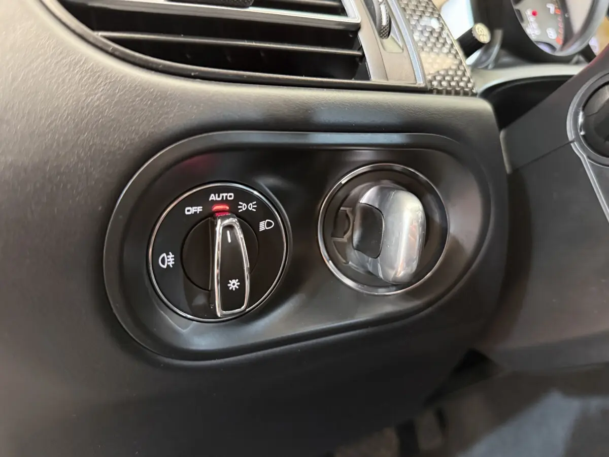 Gros plan sur la commande des phares et l'aération côté gauche du tableau de bord noir du Porsche Macan 3.0 S 2019.