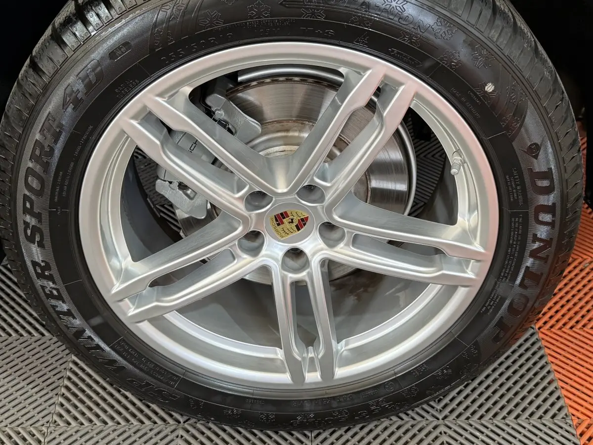 Gros plan sur la jante alu argentée avec logo Porsche au centre, montée sur pneu Dunlop hiver.