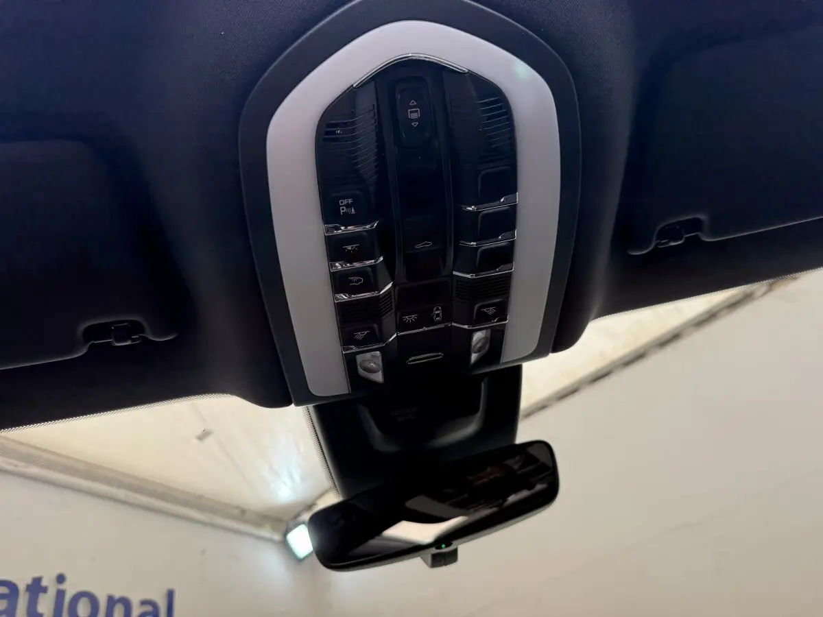 Vue en contre-plongée du panneau de commandes au plafond noir du Porsche Macan 3.0 S gris foncé, avec rétroviseur intérieur visible.