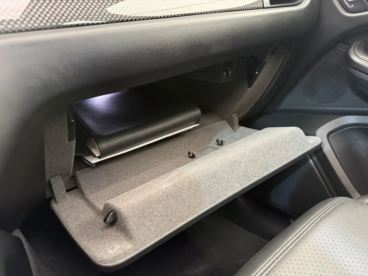 Vue intérieure côté passager du coffre à gants ouvert du Porsche Macan 3.0 S gris foncé avec dossier de siège en cuir perforé.