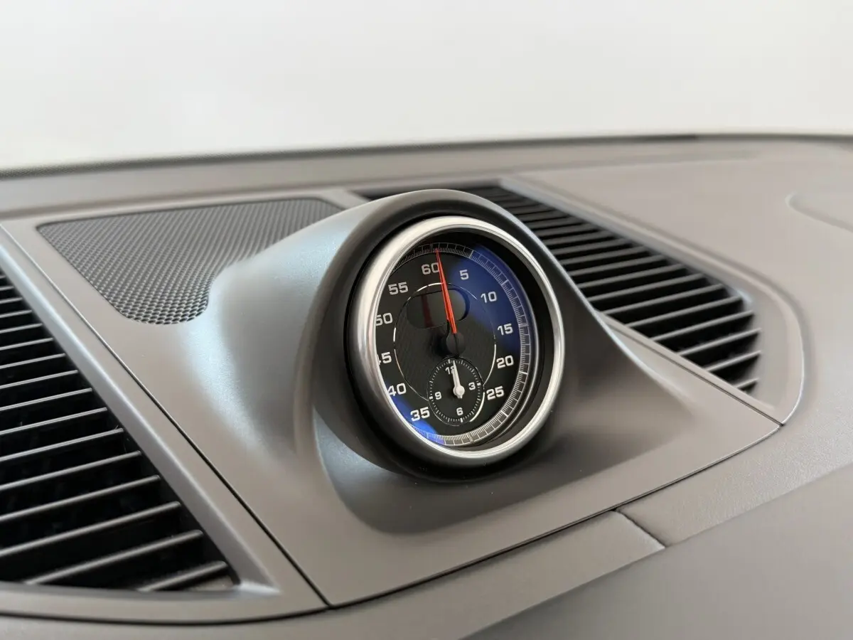 Gros plan sur l'horloge centrale du tableau de bord du Porsche Macan 3.0 S gris foncé, intérieur épuré et moderne.