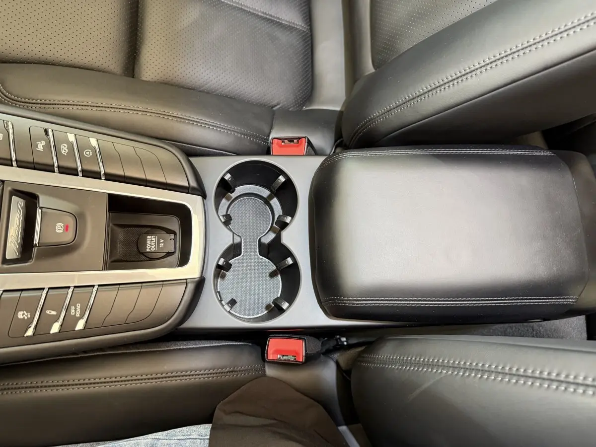 Vue plongeante sur la console centrale noire du Porsche Macan 3.0 S avec porte-gobelets et accoudoir cuir.