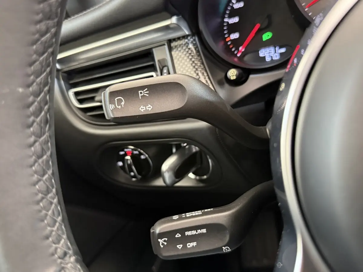 Gros plan sur les commandes au volant en cuir du Porsche Macan 3.0 S gris foncé, affichage du tableau de bord partiel visible.
