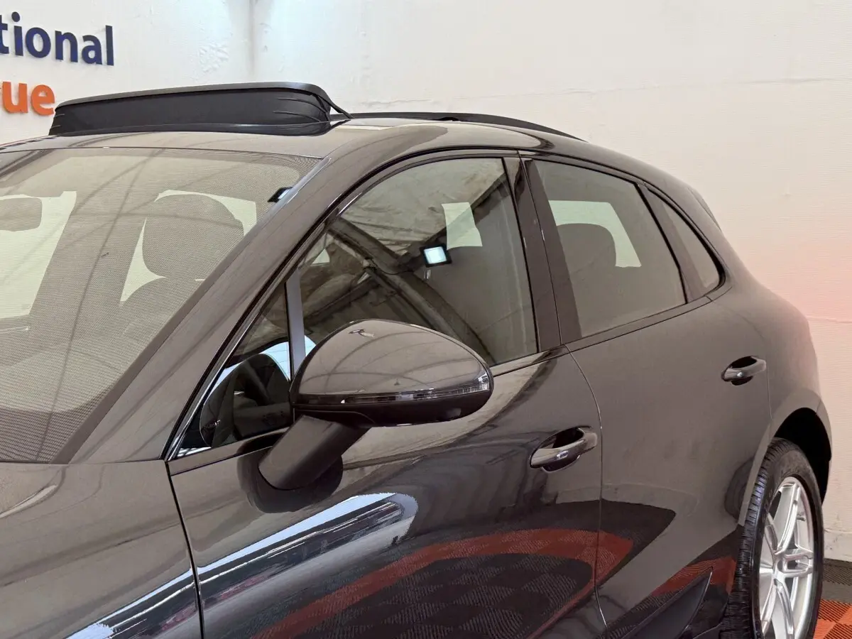 Vue latérale côté gauche d’un Porsche Macan 3.0 S gris foncé avec rétroviseur et poignées de porte visibles.