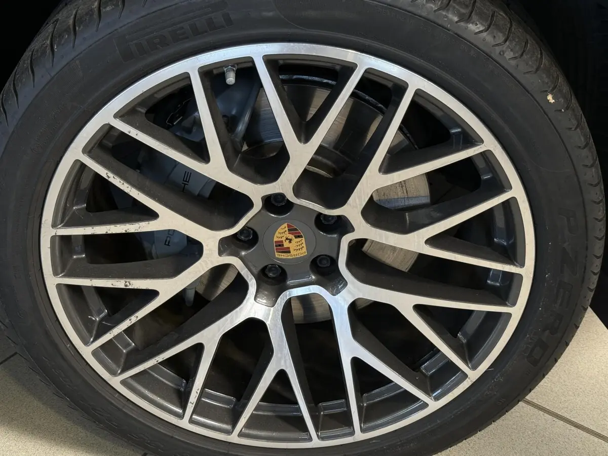 Gros plan sur la jante alliage bicolore et le logo Porsche au centre du pneu Pirelli d’un Macan gris foncé.