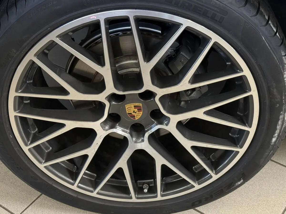Gros plan sur la jante alliage bicolore avec logo Porsche au centre, montée sur pneu Pirelli.
