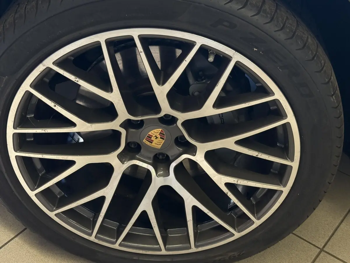 Gros plan sur la jante alliage bicolore d'une Porsche Macan 3.0 S gris foncé avec logo Porsche au centre.