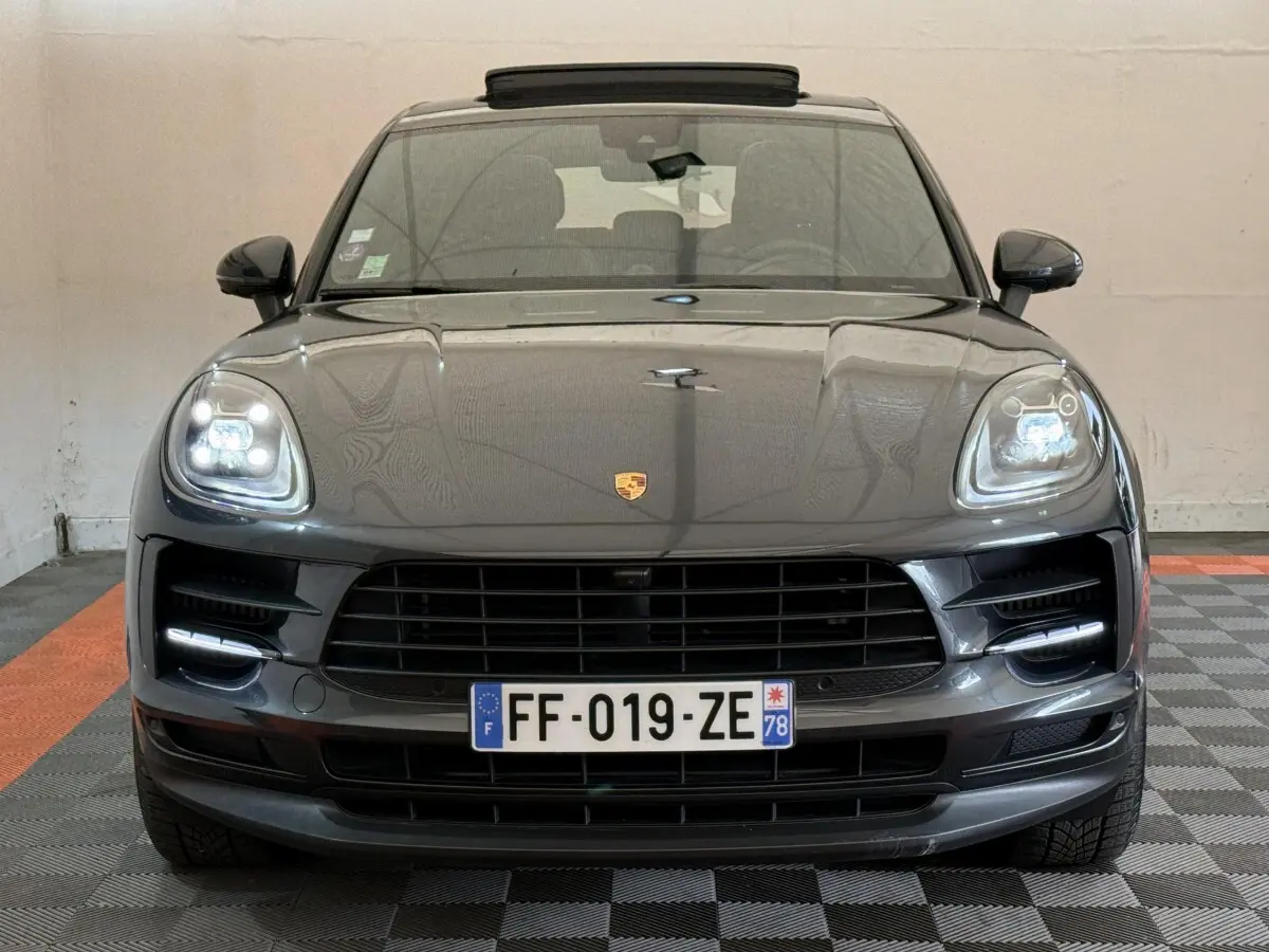 Vue frontale d’un Porsche Macan 3.0 S gris foncé avec phares LED allumés et calandre noire dans un garage.