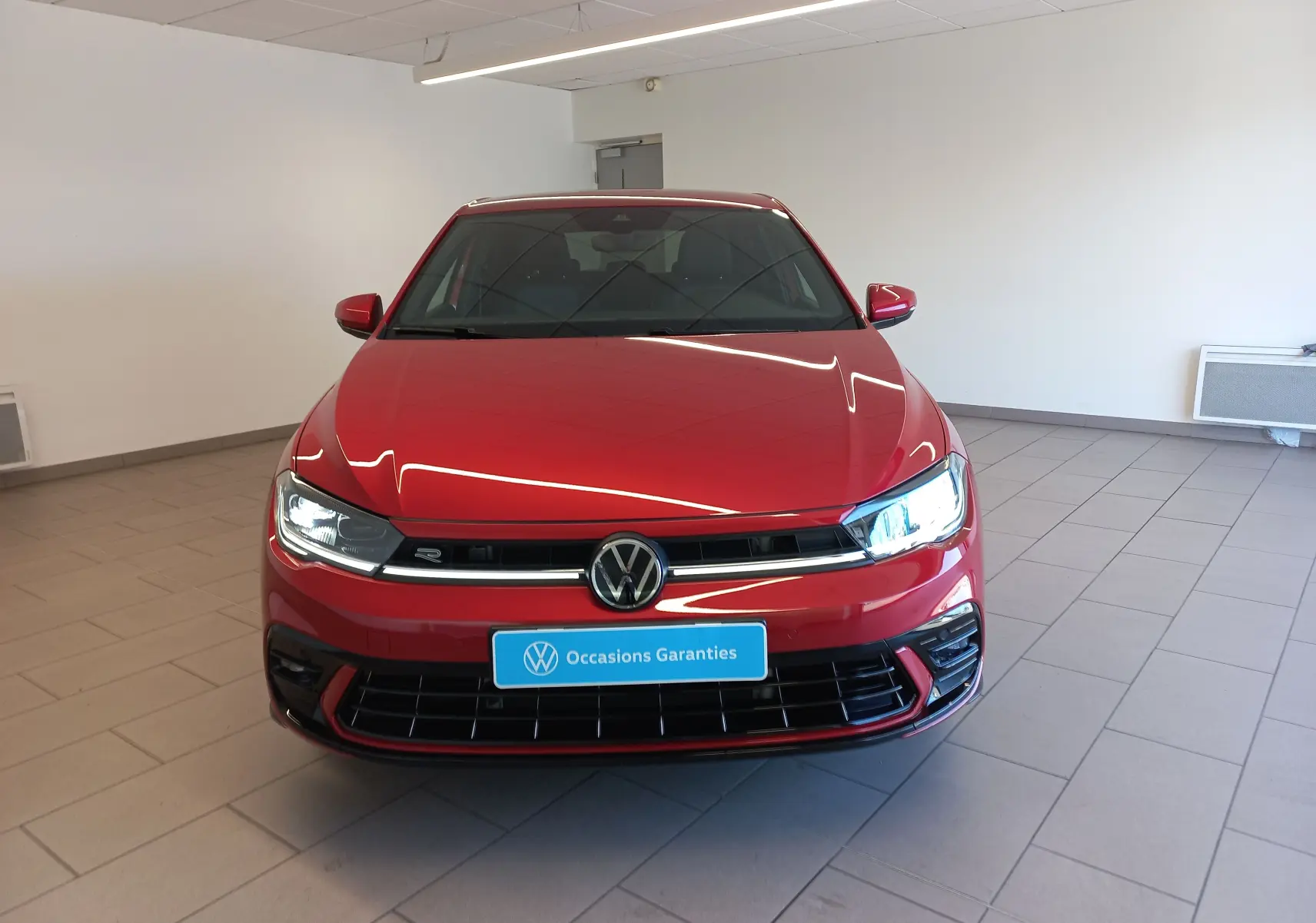 Volkswagen Polo 1.0 TSI R-Line Edition rouge Roi vue de face en intérieur avec phares allumés.