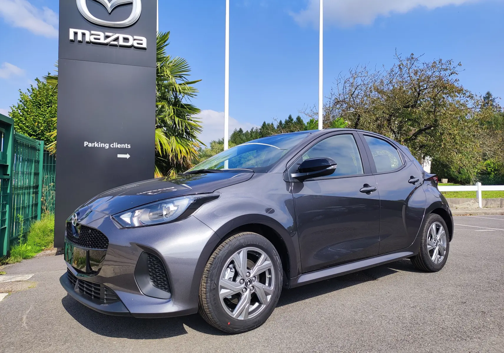 Vue 3/4 avant d'une Mazda2 gris foncé 2024 hybride, avec jantes alliage et calandre noire brillante.