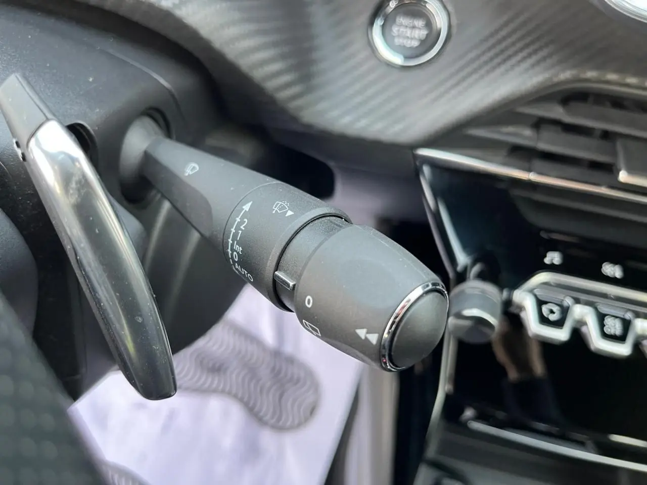 Gros plan sur la commande des essuie-glaces et le bouton start/stop dans l'habitacle du Peugeot 2008 gris avec toit noir.