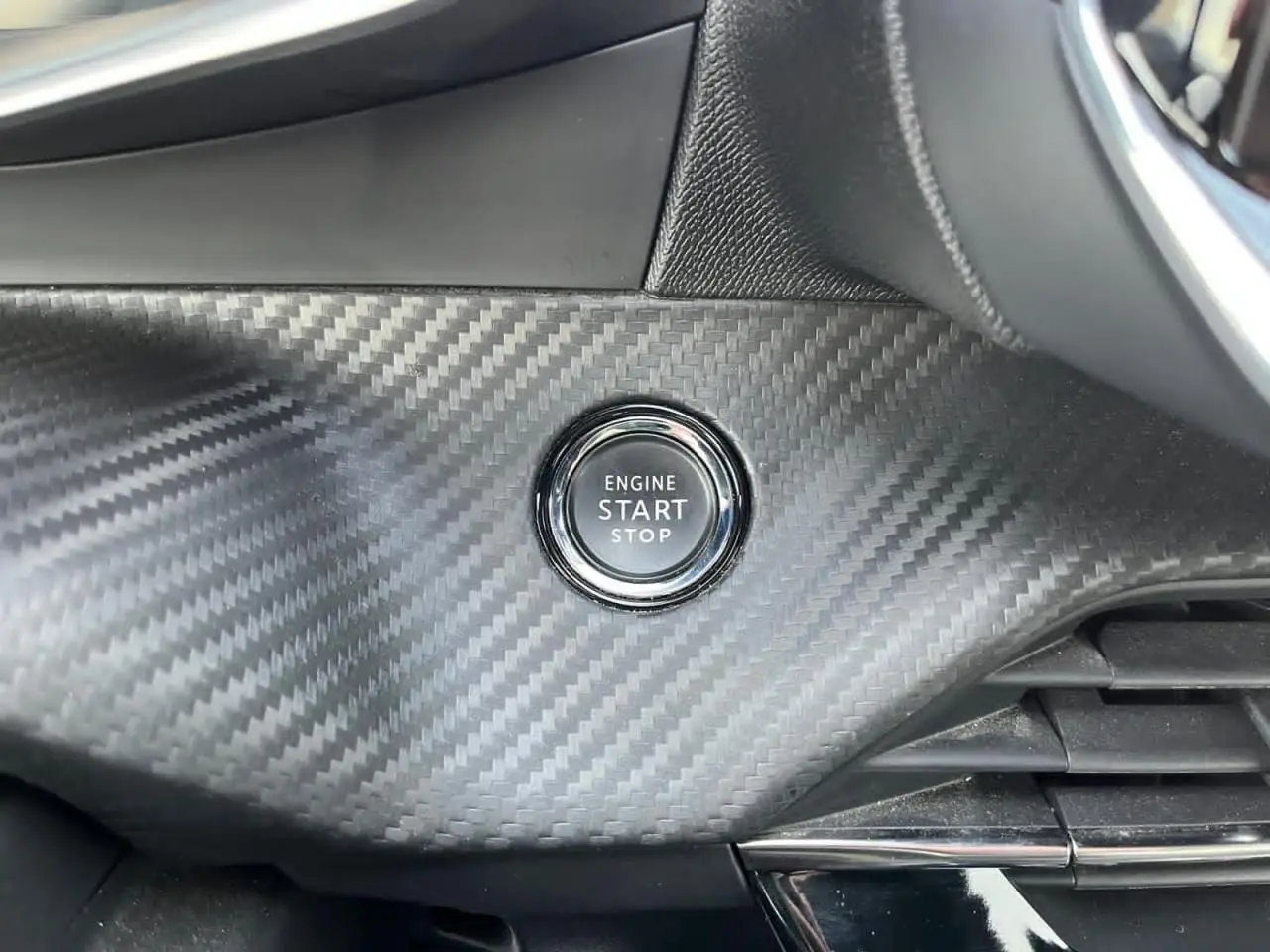 Bouton start/stop sur tableau de bord effet carbone du Peugeot 2008 II GT avec finition intérieure noire.
