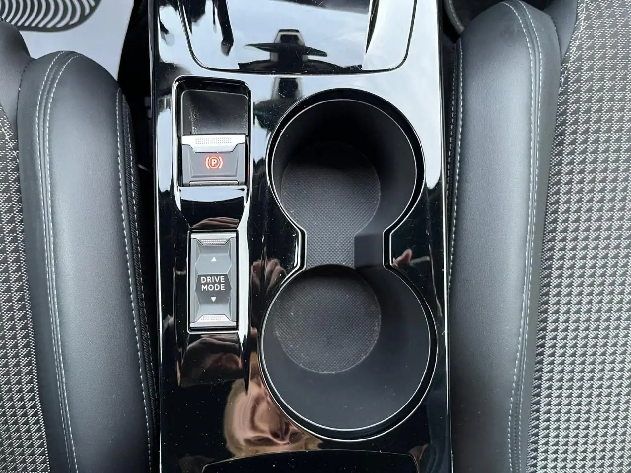 Gros plan sur la console centrale noire brillante avec porte-gobelets et commandes Drive Mode du Peugeot 2008 gris Artense.
