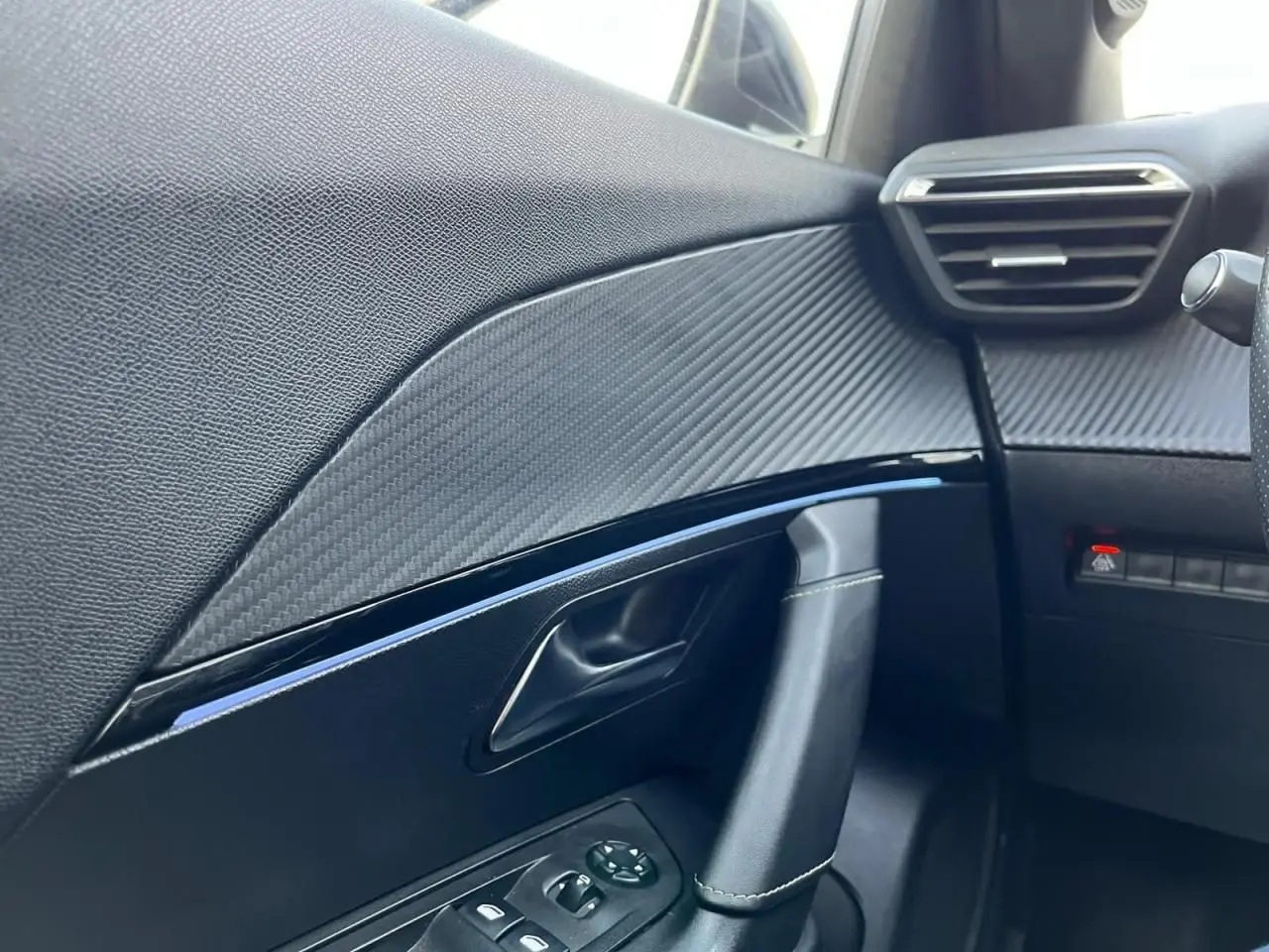 Détail intérieur côté gauche de la porte Peugeot 2008 gris Artense, avec garniture effet carbone et commandes de vitres.