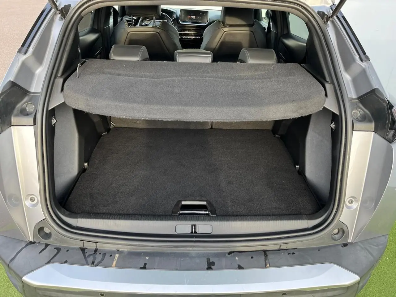 Coffre ouvert vu de l'arrière d'un Peugeot 2008 gris Artense avec intérieur noir et tablette cache-bagages déployée.