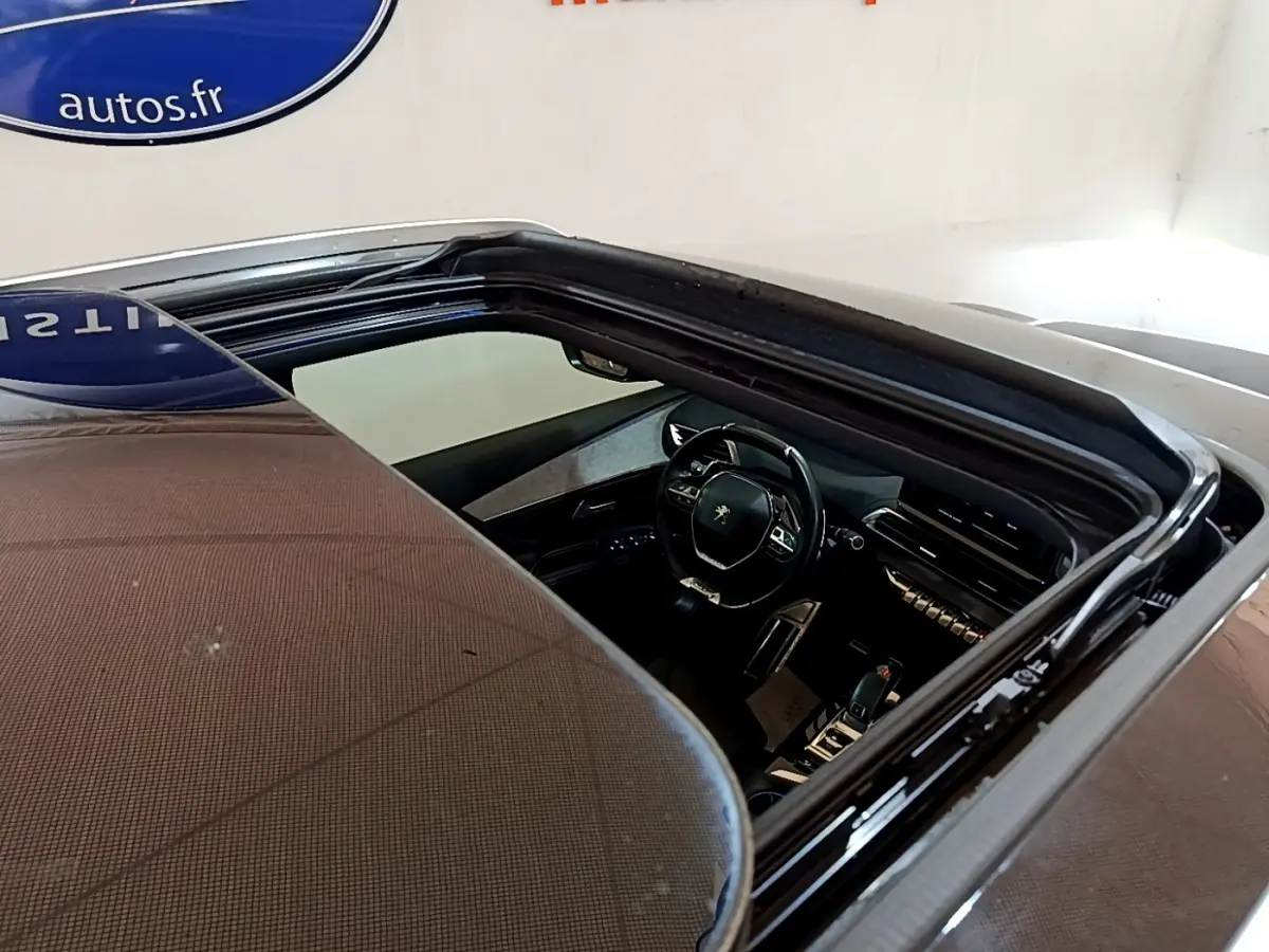 Vue plongeante sur l'intérieur noir du Peugeot 5008 bleu, mettant en valeur le volant et le tableau de bord moderne.