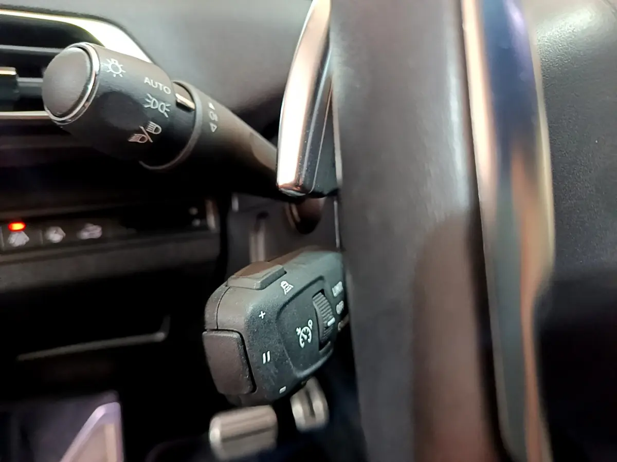 Gros plan sur les commandes au volant et levier d’éclairage du Peugeot 5008 GT 2021, intérieur noir.