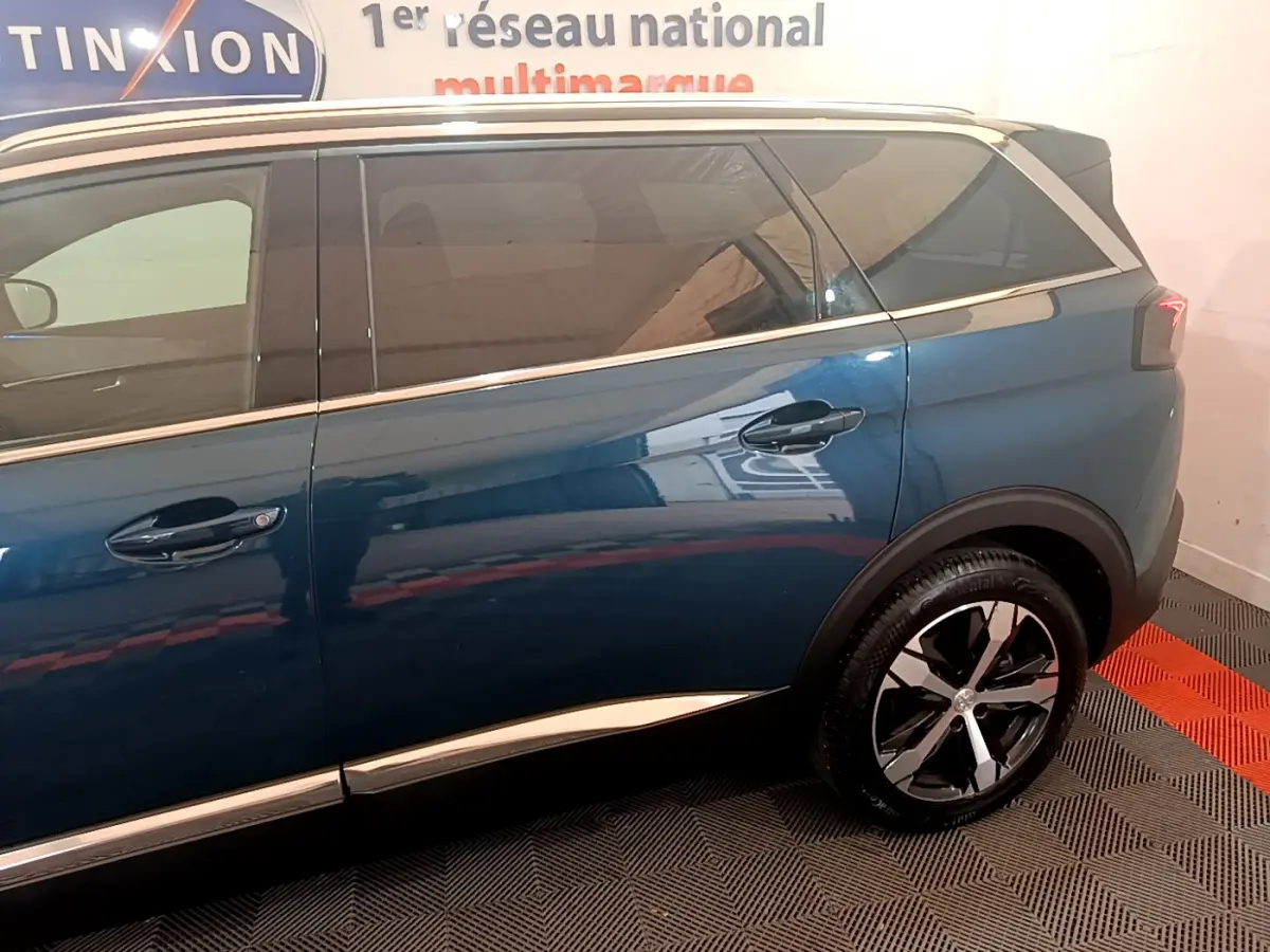Vue latérale droite du Peugeot 5008 bleu avec jantes alliage et vitres teintées dans un showroom intérieur.
